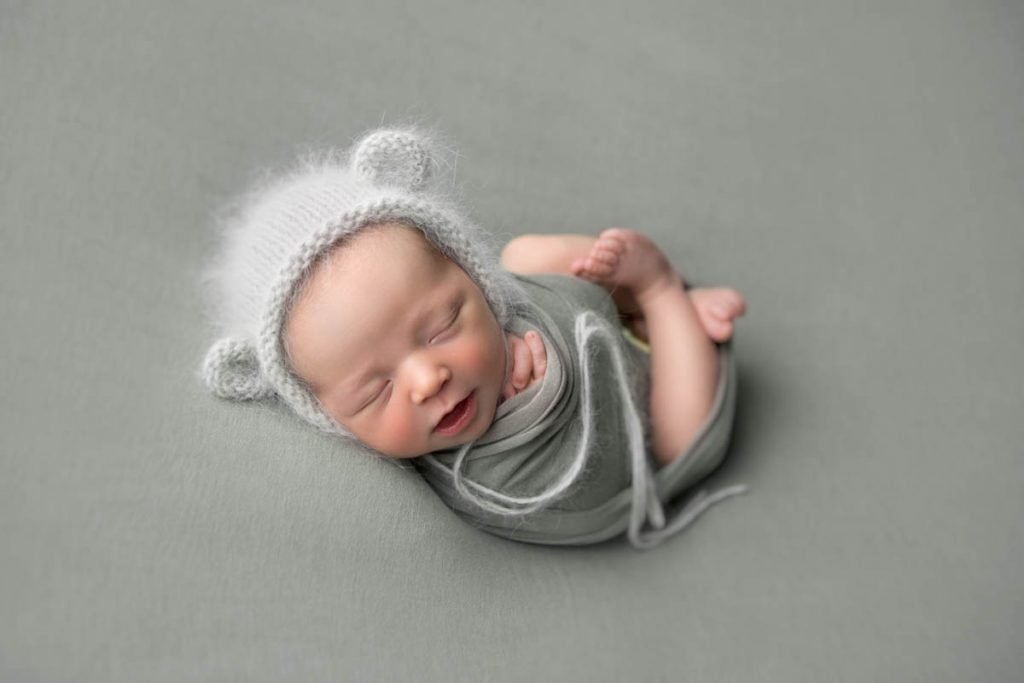 newborn baby boy swaddled in teddy bear hat.