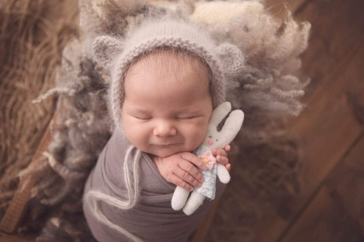 newborn sleeping girl smiling holding teddy bear