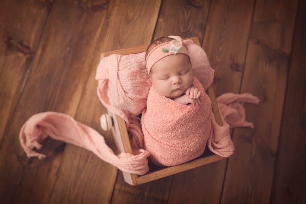 Newborn girl swaddled in pink wrap, sleeping in vintage drawer