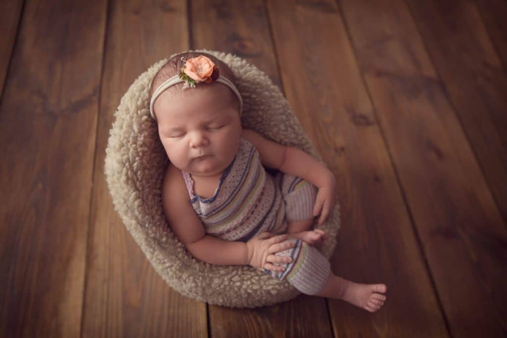 Newborn baby girl sleeping in using chair wearing dungarees
