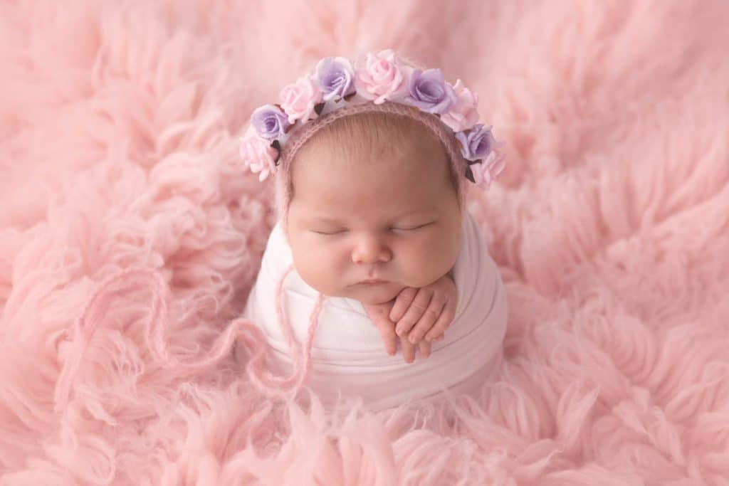 Newborn baby girl in potato sack pose on pink rug