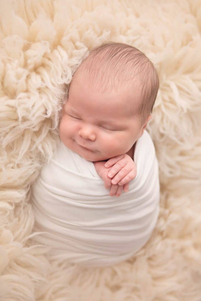 Newborn baby girl sleeping on cream flokati rug